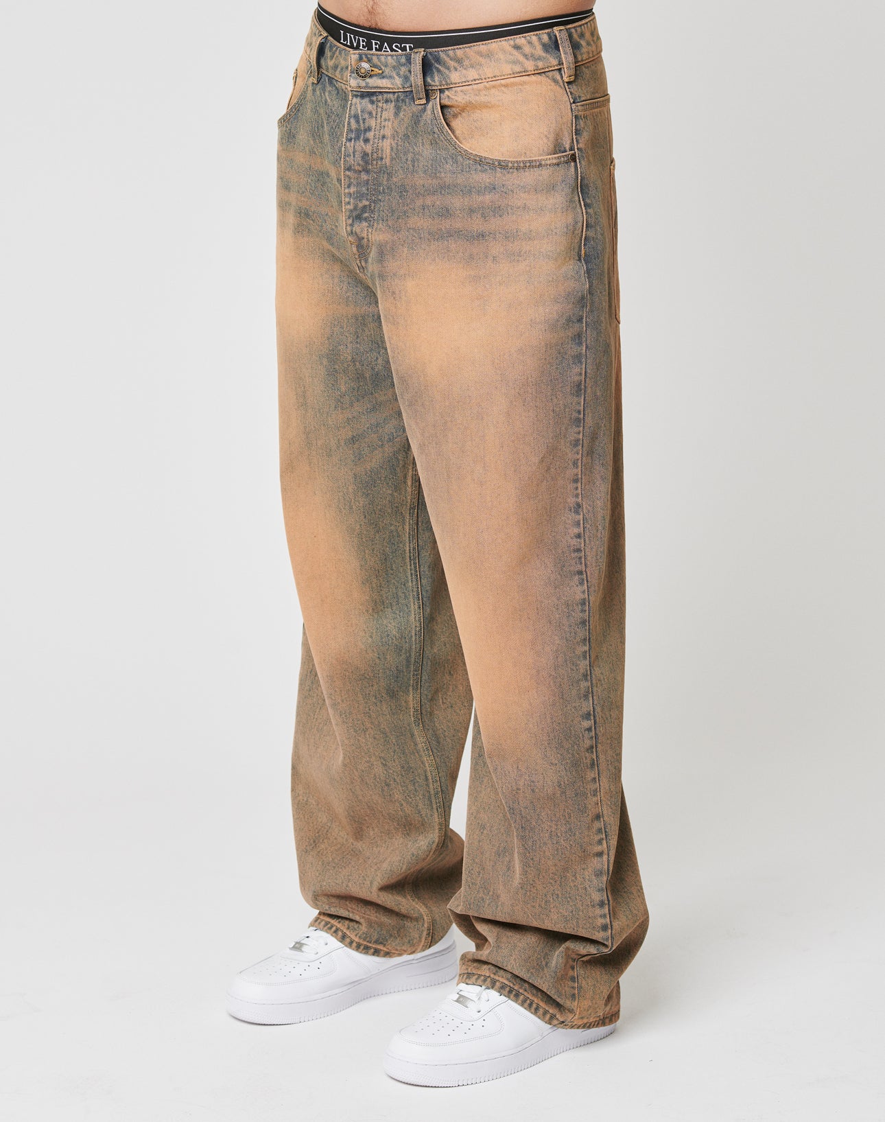 Wearing LFDY Baggy Denim by LIVE FAST DIE YOUNGāloose, high-waisted, faded brown and blue 100% Baumwolle jeans with a weites gerades Bein, baggy fit, and distressed lookāpaired with white sneakers. Upper body not visible.