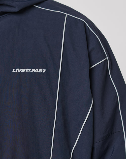 Close-up of the Live Fast Trackjacket by LIVE FAST DIE YOUNG featuring navy blue fabric, white piping, reflective LIVE FAST print on the chest, and elastic cuffs for comfort.
