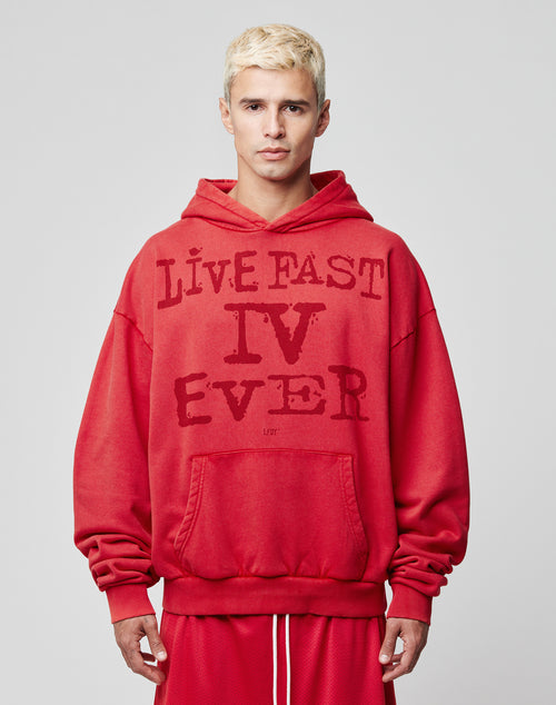 A person with short, bleach-blond hair wears the LIVE FAST DIE YOUNG LFDY IV Ever Hooded, an oversize-fit red hoodie with LIVE FAST IV EVER in bold. Made from 100% Baumwolle and vintage washed, they face forward against a light gray background.
