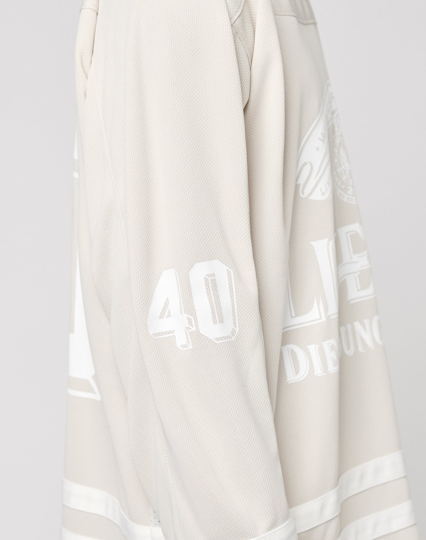 A close-up shows part of the upper body wearing the LFDY Hockey Jersey by LIVE FAST DIE YOUNG in light beige, featuring a number 40 Ärmelprint, white lettering, textured polyester fabric, and an oversized fit.