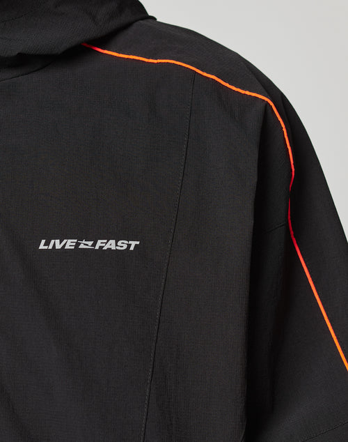 The Live Fast Trackjacket from LIVE FAST DIE YOUNG is a black nylon jacket with LIVE FAST in reflective print on the chest, a bright orange stripe along the shoulder and sleeve, and elastic cuffs for a comfortable fit.