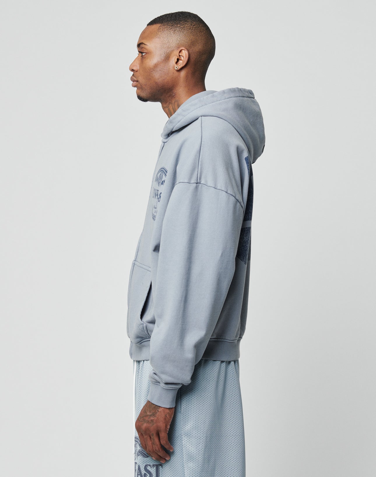 A man in profile wears the LIVE FAST DIE YOUNG LFDY 55 Hooded Zip, a light blue oversized hoodie, with matching mesh shorts against a plain white background.