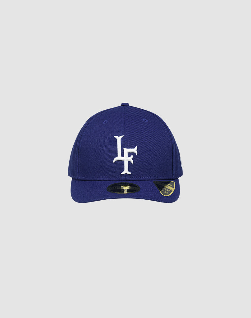 The LFDY X NEW ERA 59FIFTY LOW PROFILE fitted cap by LIVE FAST DIE YOUNG is blue with a white LF logo on the front, low profile design, and a shiny brim sticker. Shown on a plain light gray background.