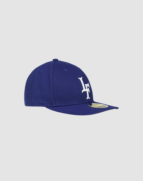 The LFDY X NEW ERA 59FIFTY LOW PROFILE by LIVE FAST DIE YOUNG is a royal blue fitted cap with a white LF logo, gold sticker on the flat brim, and low profile silhouette, shown against a light gray background.