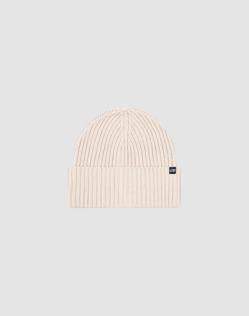 The LIVE FAST DIE YOUNG Rib Knit Beanie in light beige features a ribbed knit, folded brim with a black and white Flag-Label, and is made from a durable, comfortable polyamide blend. Shown on a plain gray background. One Size.