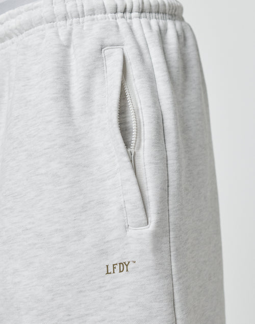Close-up of the Basic Loose Jogger by LIVE FAST DIE YOUNG in light gray, showing a pocket with a white zipper and elastic waistband, plus gold embroidered LFDY logo near the pocket.