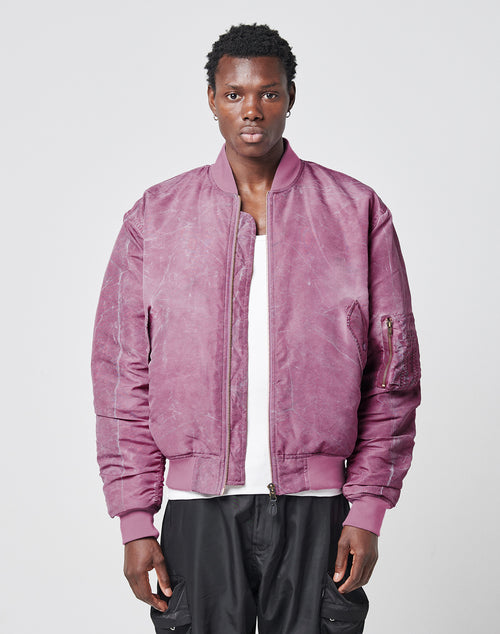 A person faces forward, wearing the LIVE FAST DIE YOUNG Washed Bomber Jacket in dusty pink over a white shirt and black pants, standing against a plain light gray background.