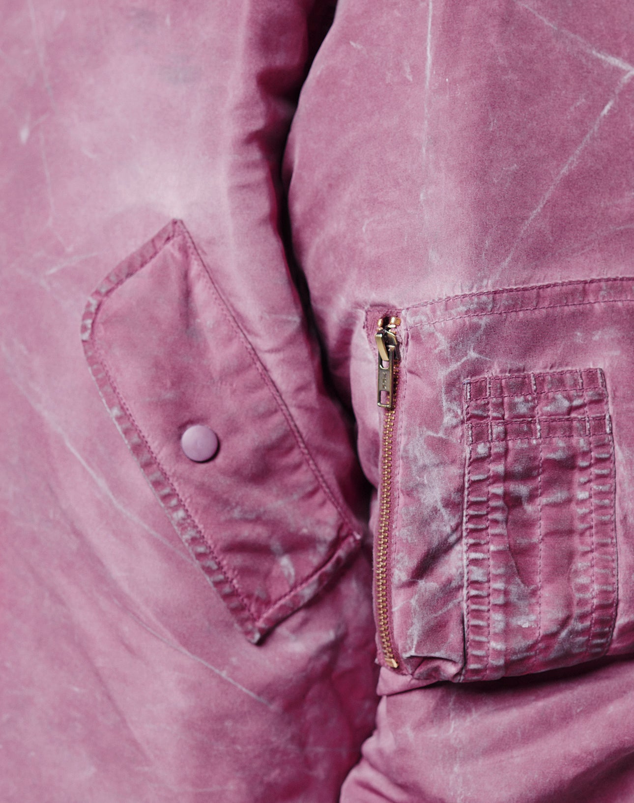 Close-up of the Washed Bomber Jacket by LIVE FAST DIE YOUNG, featuring a mauve hue, flap pocket, button, zippered sleeve pocket with Leder Puller, and vintage-washed textured fabric.