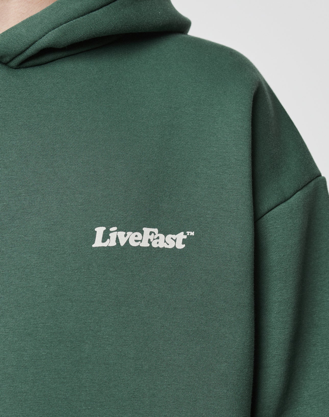 Close-up of the dark green Basic 360 Hooded by LIVE FAST DIE YOUNG, featuring LiveFast⢠in white on the chest. Made from a soft cotton-polyester blend; image shows the upper left section without revealing the wearerās face.