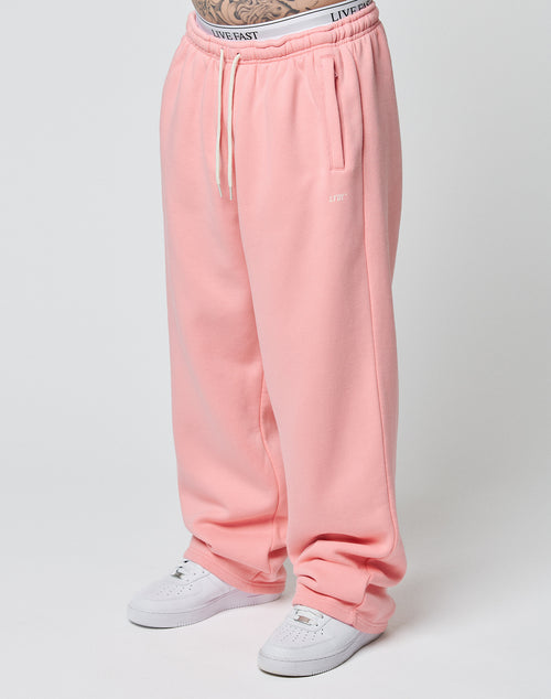 A person wearing LIVE FAST DIE YOUNG Basic Wide Jogger sweatpants in pink with white drawstrings and white sneakers, standing against a plain light background. Only their lower body is visible.
