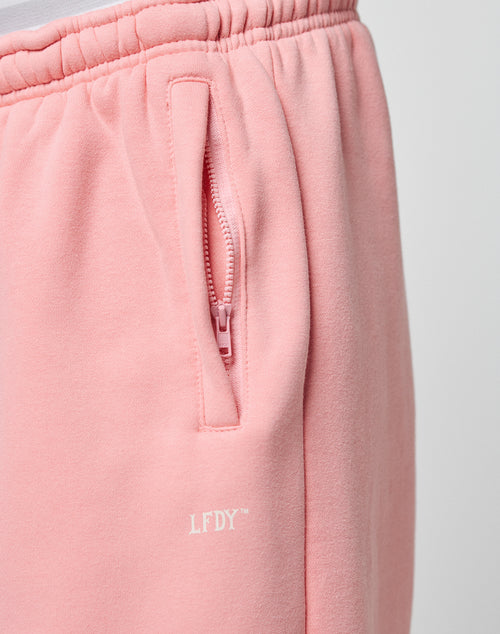 Close-up of the LIVE FAST DIE YOUNG Basic Wide Jogger in light pink, featuring an elastic waistband, zippered side pocket, and a bold white logo print below the pocket.