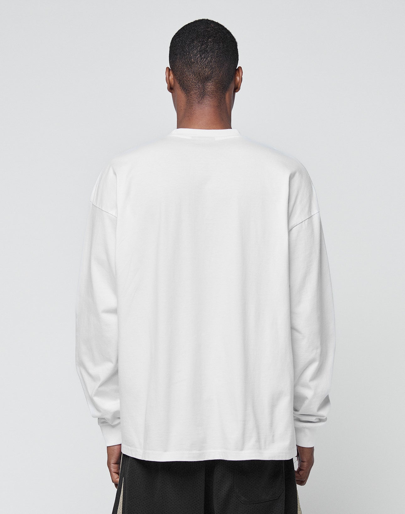 A person with short hair, seen from behind, is wearing a loose Basic Longsleeve by LIVE FAST DIE YOUNG and black shorts against a plain light gray background.