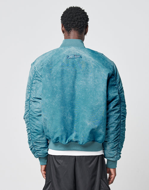 A person with short curly hair wears the LIVE FAST DIE YOUNG Washed Bomber Jacket, featuring a Leder Puller, and black pants, standing with their back to the camera against a plain light gray background.