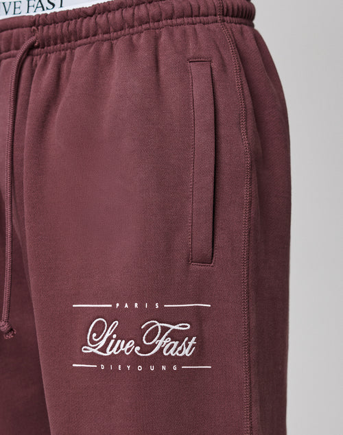 Close-up of maroon Wide Cuff Jogger by LIVE FAST DIE YOUNG, featuring a pocket and PARIS LIVE FAST DIE YOUNG printed in white near the left thigh. Wide fit with waistband showing LIVE FAST text at the top.