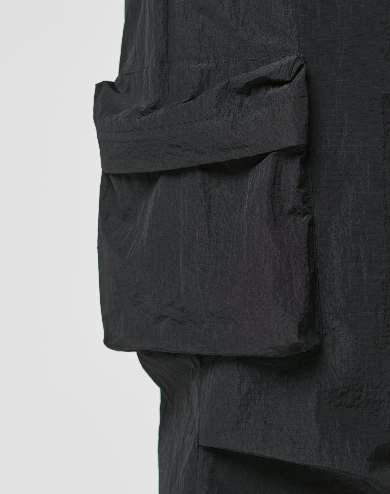 Close-up of textured black fabric with a large rectangular Cargotasche sewn on, part of LIVE FAST DIE YOUNG’s Live Fast Nylon Pants, shown against a plain light background.