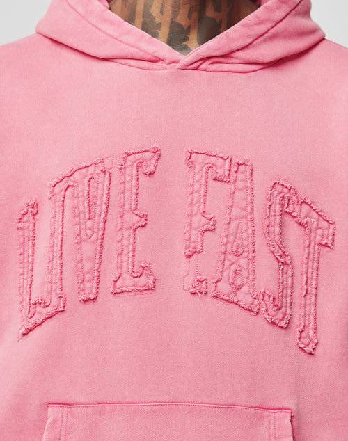 A close-up of the pink Ripped College Hooded by LIVE FAST DIE YOUNG, featuring distressed “LIVE FAST” letters on the chest and 100% Baumwolle fabric, with part of a tattooed neck visible above the oversize fit hoodie.