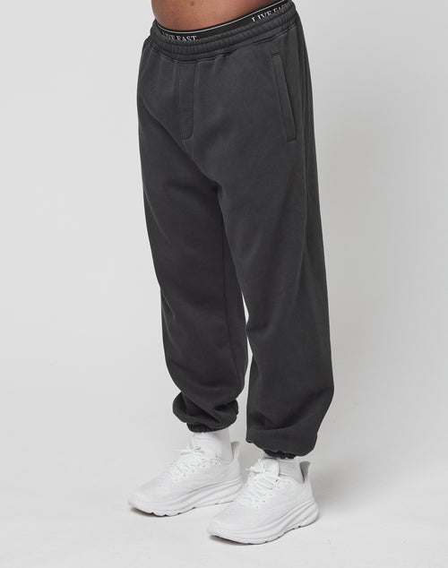 Eine Person trägt schwarze LFDY Sphere Jogger von LIVE FAST DIE YOUNG mit Elastikbund und seitlichen Taschen sowie weiße Sneakers vor weißem Hintergrund. Sichtbar ist nur die untere Körperhälfte.