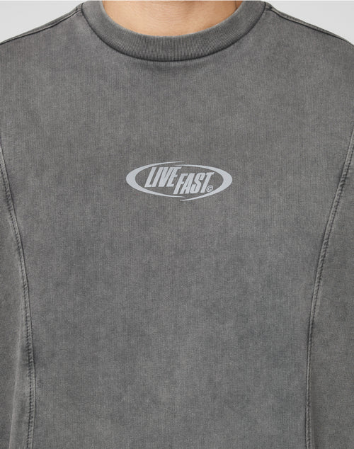 A close-up shows a person wearing the Live Fast Wave Tee by LIVE FAST DIE YOUNG, an Oversize Fit faded gray sweatshirt with a reflective oval-shaped chest print reading LIVE FAST. The persons face is not visible.