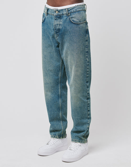 Wearing LIVE FAST DIE YOUNG Regular Denim blue jeans, made from recycled cotton with a regular fit and tapered leg, paired with white sneakers. Only the lower torso and legs appear against a plain white background.