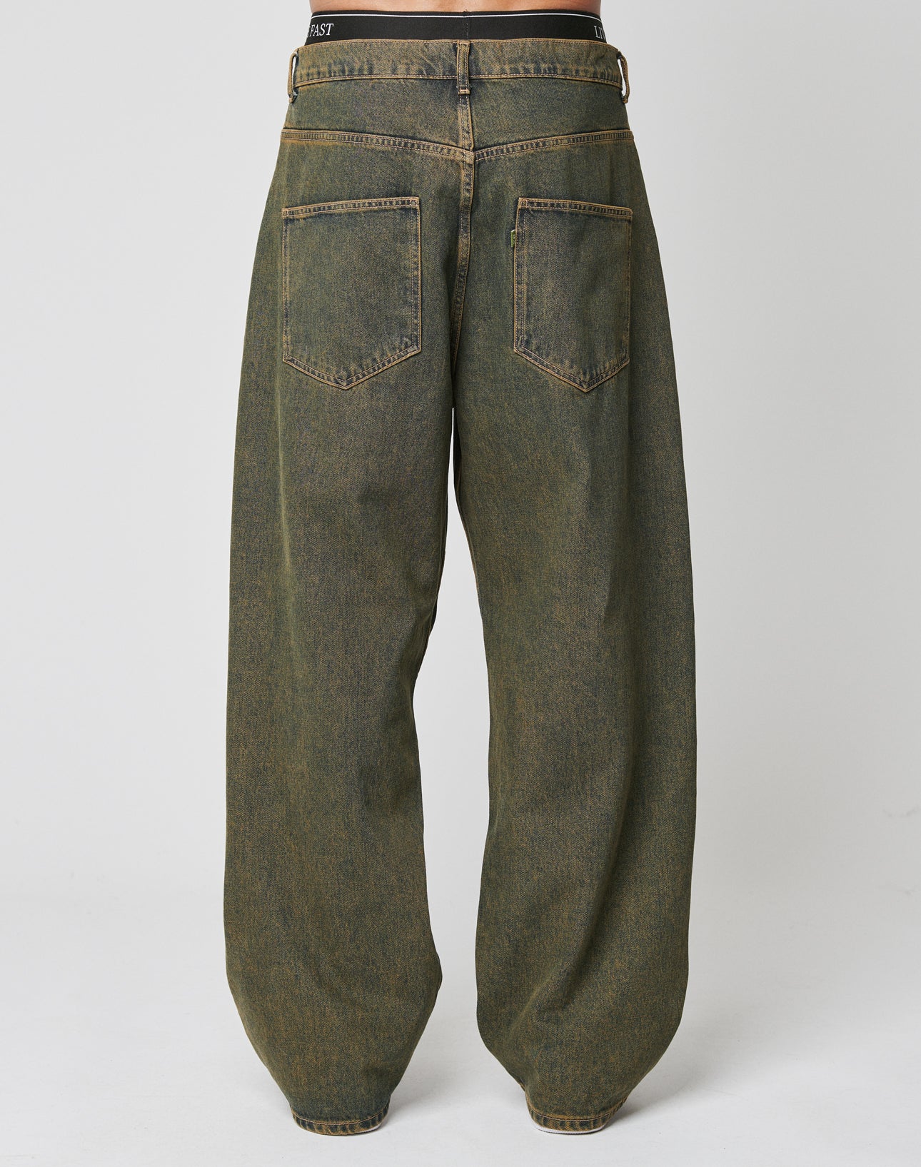 A person is shown from the back in LIVE FAST DIE YOUNGās LFDY Baggy Denimābaggy fit, dark greenish-brown, high-waisted jeans with large back pockets, made from 100% Baumwolle, set against a plain light background.