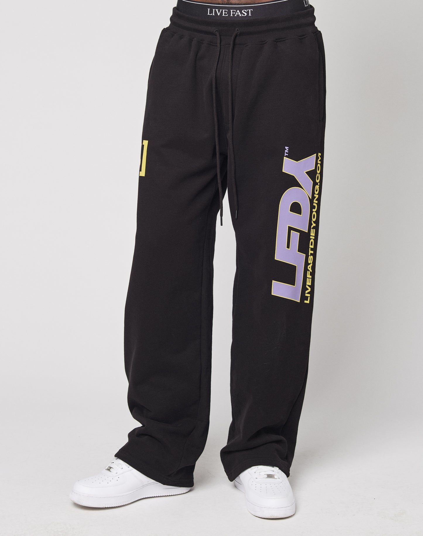 Model wears the LFDY Racing Wide Jogger by LIVE FAST DIE YOUNG in black, featuring bold branding and an elastikbund, made from comfortable baumwolle. Styled with white sneakers against a plain backdrop.