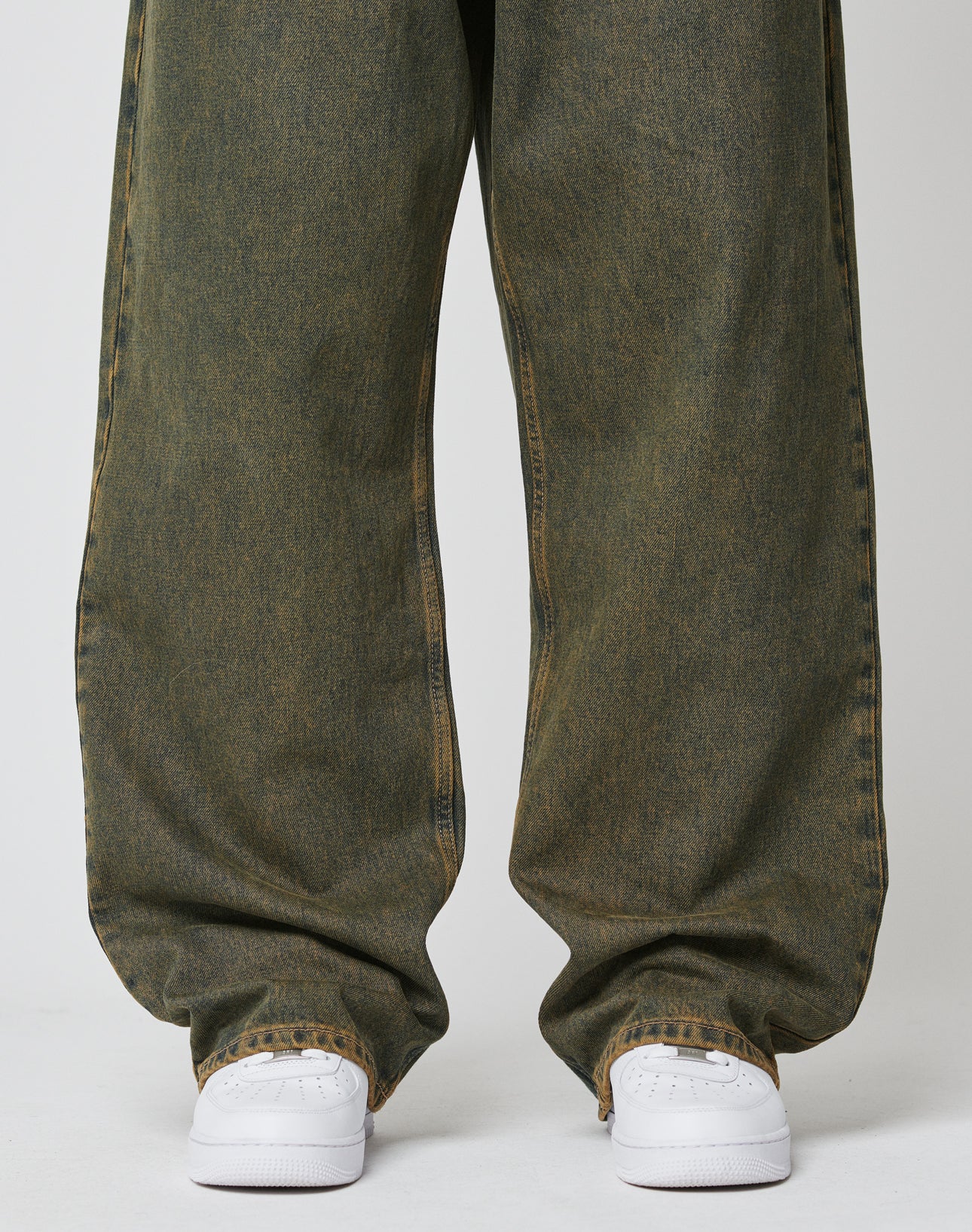 A person wears LFDY Baggy Denim by LIVE FAST DIE YOUNGābaggy fit, faded green jeans with a wide straight leg made from 100% cottonābunching at the ankles over white sneakers on a plain white background.