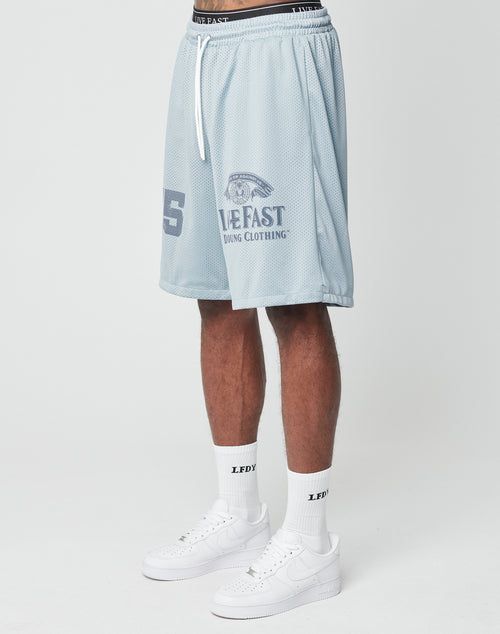 A person in light blue LFDY Loyal Shorts by LIVE FAST DIE YOUNG with an oversized fit and elastic waistband, paired with white LFDY socks and white Nike sneakers, stands against a plain white background.