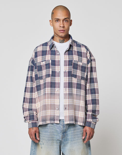 A person stands facing forward against a plain light gray background, wearing the LIVE FAST DIE YOUNG Vintage Flannel—a blue, white, and red plaid shirt with Vintage Waschung and Zweiteiliger Hemdkragen—over a white t-shirt and light blue jeans.