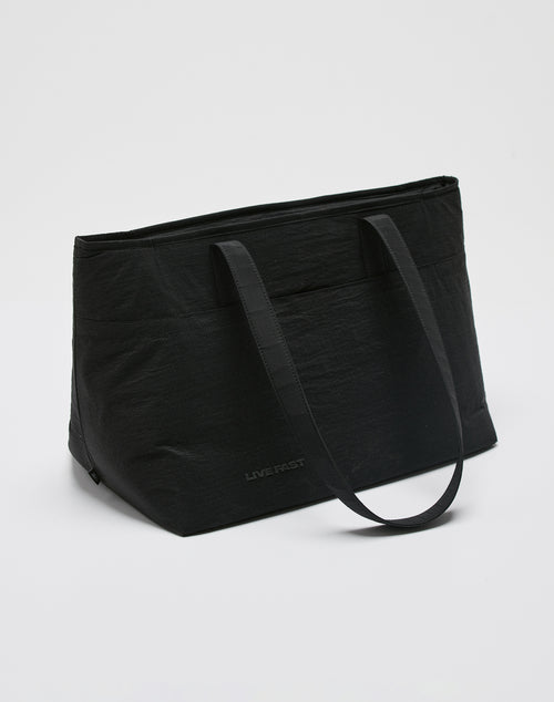 The LIVE FAST DIE YOUNG Live Fast Paintbag is a large black nylon tote with two shoulder straps, subtle LIVE FAST branding near the bottom, and a secure zip closure, shown against a plain white background.