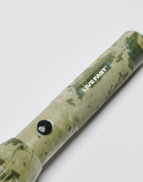 A close-up of the LIVE FAST DIE YOUNG Live Fast Flashlight, featuring an aluminium camo design, black button, and “LIVE FAST” label, set against a plain white background.