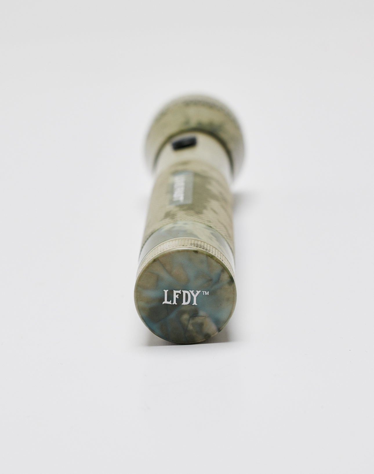 A camo-patterned aluminium Live Fast Flashlight by LIVE FAST DIE YOUNG lies on a white surface, viewed from the end with LFDY™ printed on the bottom.