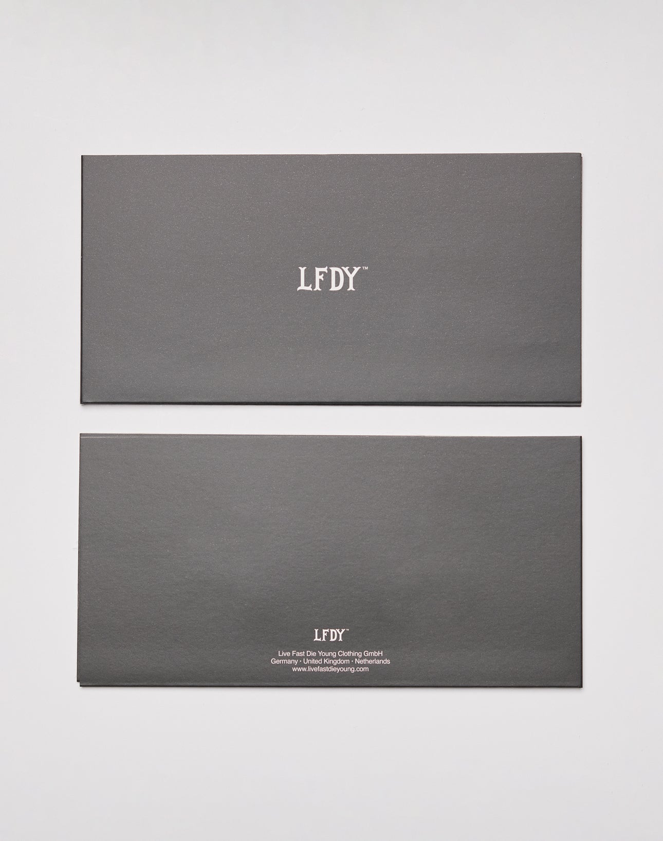 Two dark gray LIVE FAST DIE YOUNG Gutschein | Gift Card envelopes: the top shows only the white LFDY logo, while the bottom displays extra small text about a shop Gutschein Restguthaben.