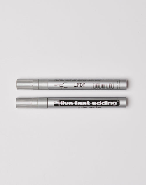 Two silver Live Fast Edding markers from LIVE FAST DIE YOUNG are laid parallel on a white surface; the top shows branding and barcode, while the bottom displays live fast edding paint marker.