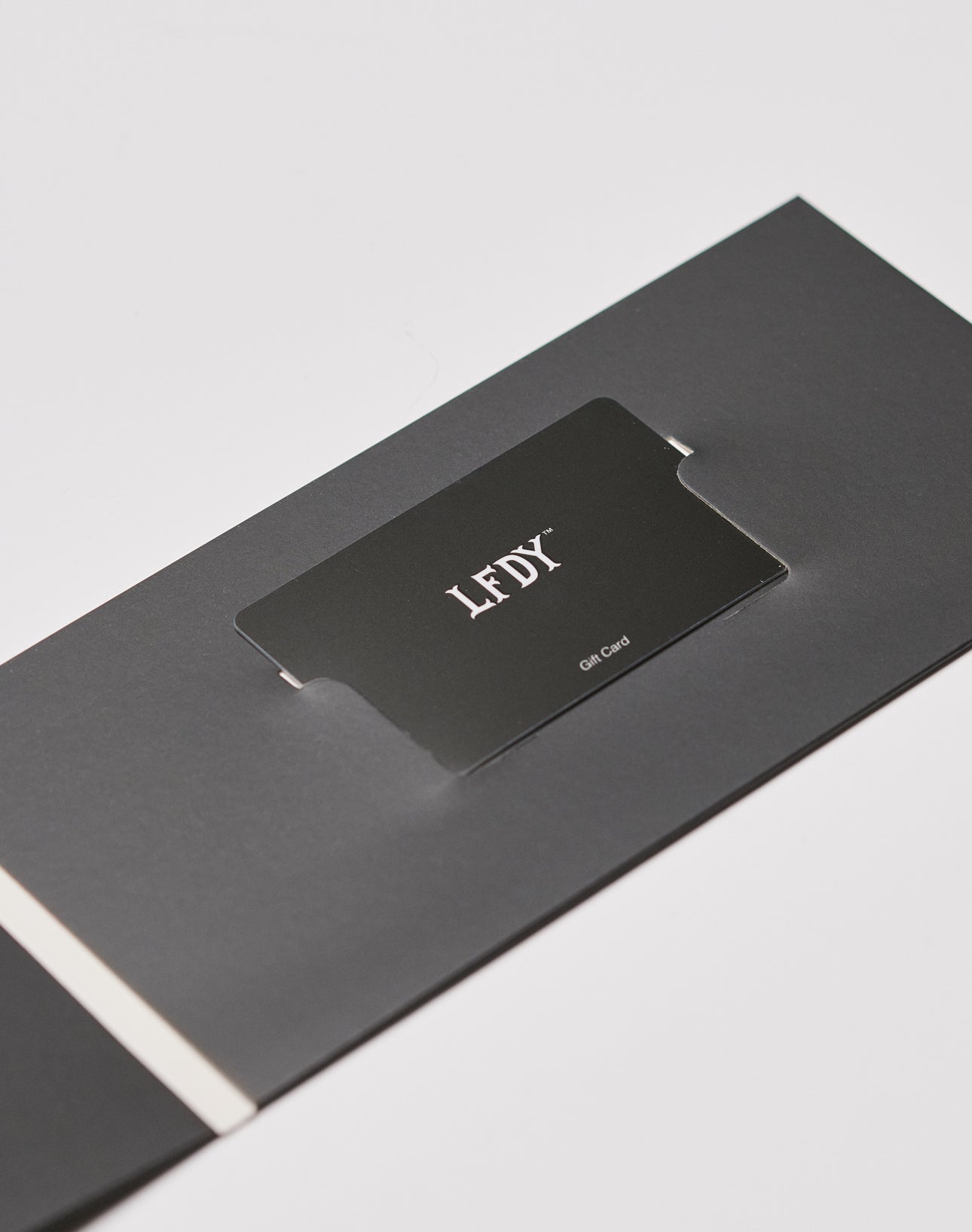 A LIVE FAST DIE YOUNG Gift Card Wrapping showcases a black gift card in a matching holder on a white background, featuring the LFDT logo in white at the center.