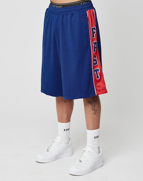 A person in LIVE FAST DIE YOUNG Striped Mesh Shorts, featuring red side stripes and an elastic waistband, plus white socks marked LEFT and white Nike sneakers, stands against a plain white background.