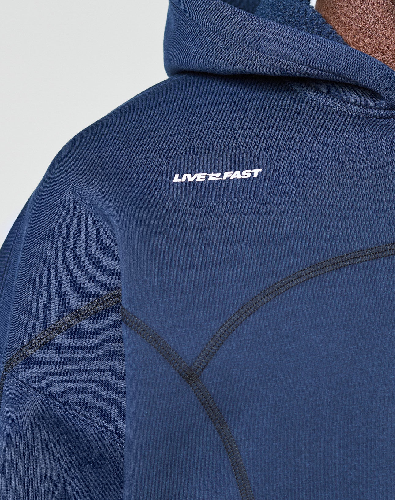A close-up of the LFDY Active Fleece Hooded Zip by LIVE FAST DIE YOUNG, an oversized navy blue hoodie with black curved stitching and a white LIVE FAST print on the chest, crafted from 100% Baumwolle for comfort and style.