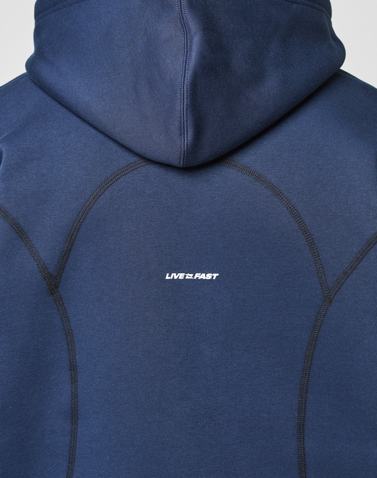 A close-up of the back of the LFDY Active Fleece Hooded Zip by LIVE FAST DIE YOUNG, an oversized navy hoodie made from 100% cotton with black stitched seams and a white LIVE 2 FAST logo print at the center.