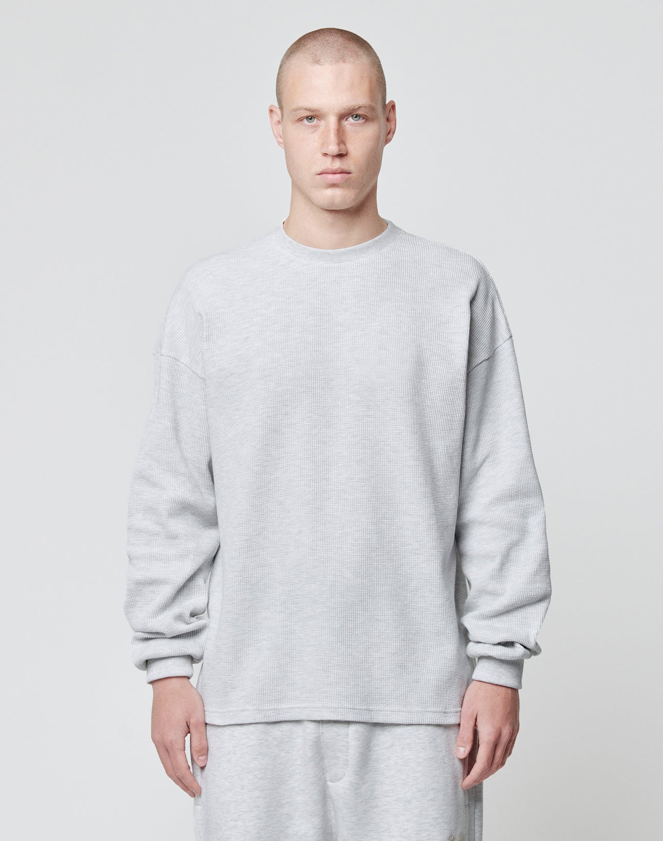 A person with a shaved head wears the LIVE FAST DIE YOUNG Blank Waffle Longsleeve in an oversize fit and light gray, paired with matching pants, made from 100% Baumwolle, standing against a plain light background.