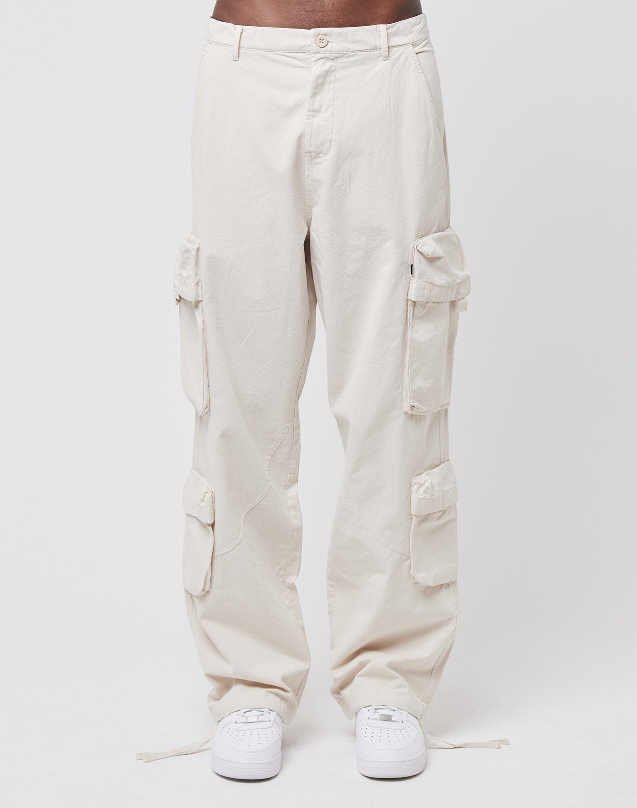 A person wearing the Wide Summer Cargo pants by LIVE FAST DIE YOUNG—a loose, light beige 100% cotton style with multiple cargo pockets—and white sneakers stands against a plain white background.
