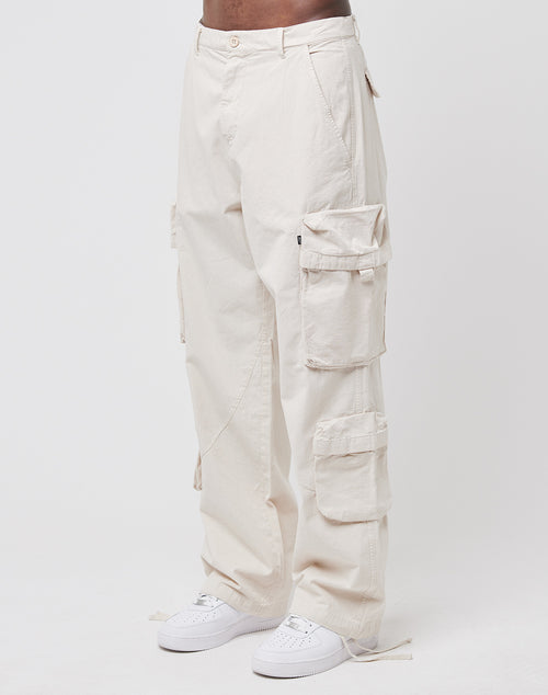 A person wears the LIVE FAST DIE YOUNG Wide Summer Cargo—loose, off-white 100% Baumwolle Ripstop pants with multiple Cargotaschen—paired with white sneakers, standing against a plain white background.
