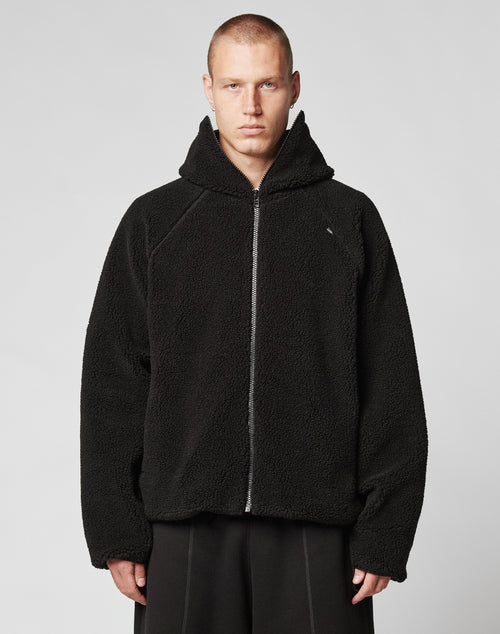 A person wears the Live Fast Teddy Jacket by LIVE FAST DIE YOUNG, featuring an oversize fit, hood with visor opening, and subtle embossed branding, standing facing forward against a plain light gray background.