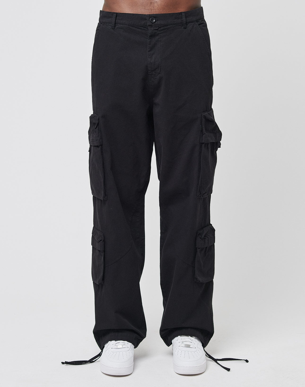 A person wearing LIVE FAST DIE YOUNG Wide Summer Cargo pants in black with multiple cargo pockets and white sneakers, standing against a plain white background.