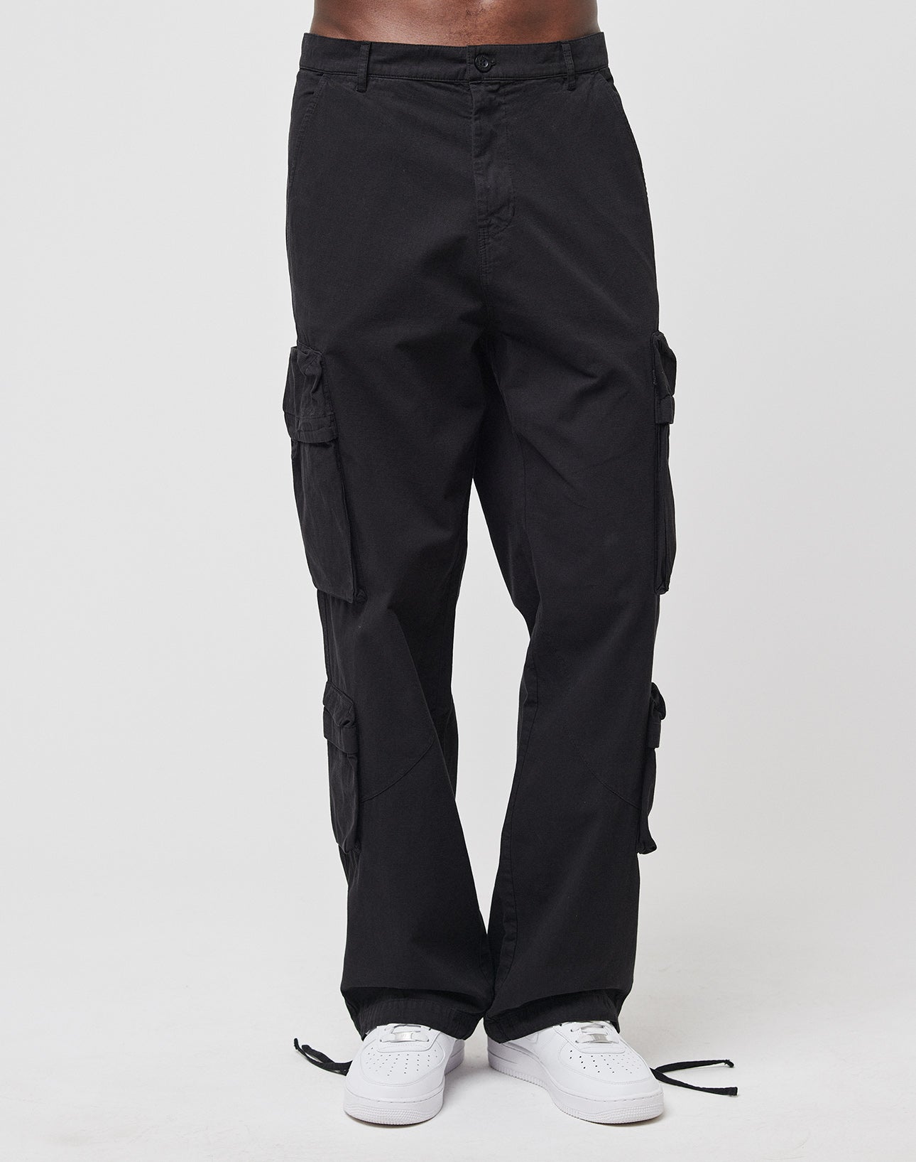 A person wears LIVE FAST DIE YOUNG Wide Summer Cargo pants with multiple cargo pockets and white sneakers, standing against a plain white background. The image is cropped at the waist, showing only the lower body.