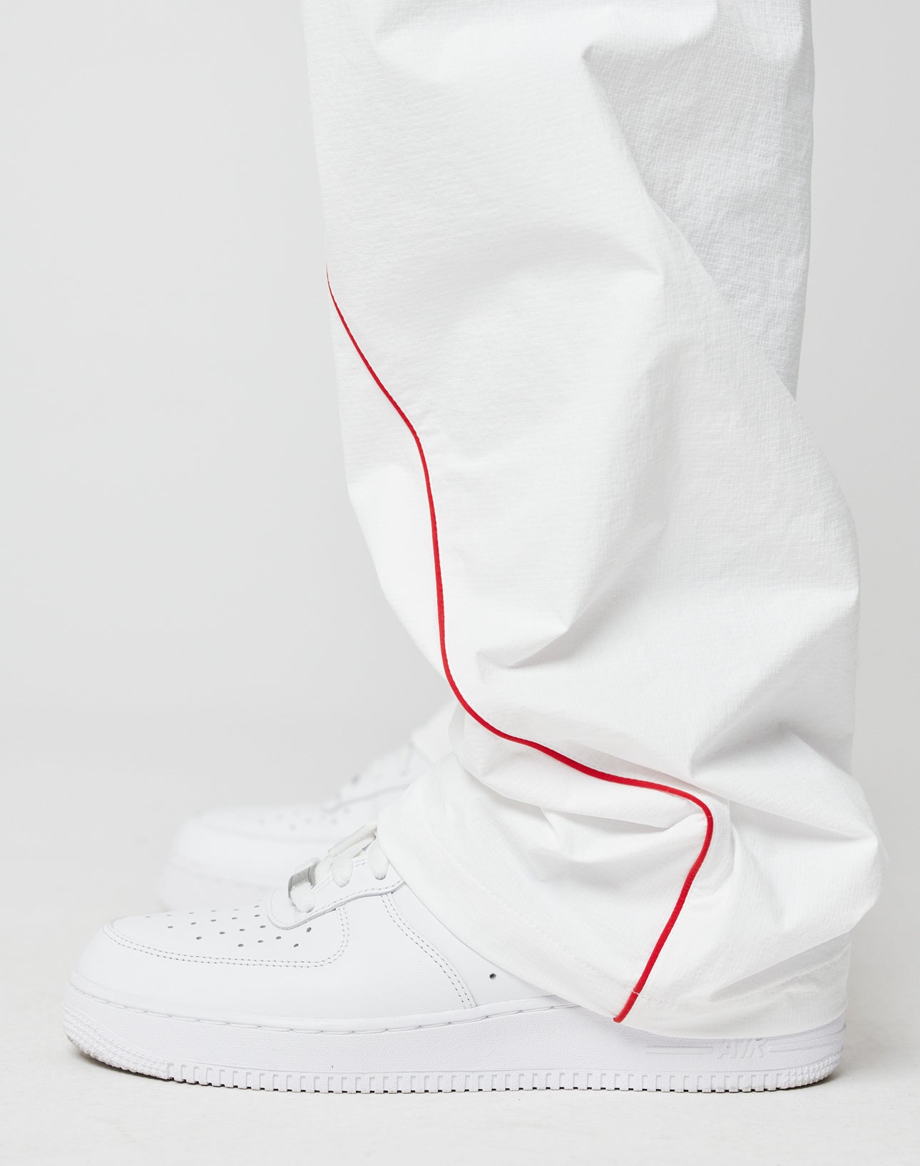 A person wearing LFDY Wavy Trackpants by LIVE FAST DIE YOUNG—wide fit, loose white pants with a red seam line—and white sneakers, standing against a plain white background.