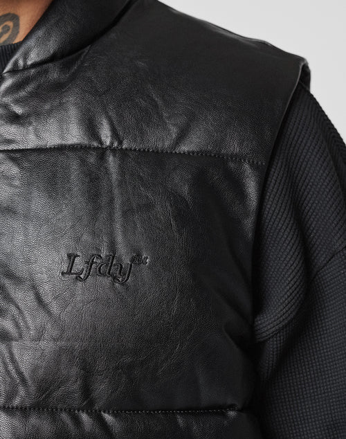 Close-up of a person wearing the LIVE FAST DIE YOUNG Padded Vest with chest embroidery and padded stand-up collar, styled over a textured black long-sleeve shirt. A neck tattoo is partially visible.