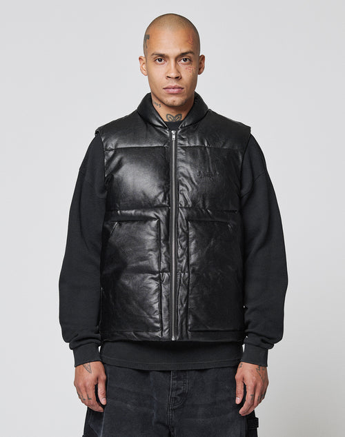 A person with a shaved head and neck tattoos wears the LIVE FAST DIE YOUNG Padded Vest over a black sweatshirt, standing against a plain light gray background.