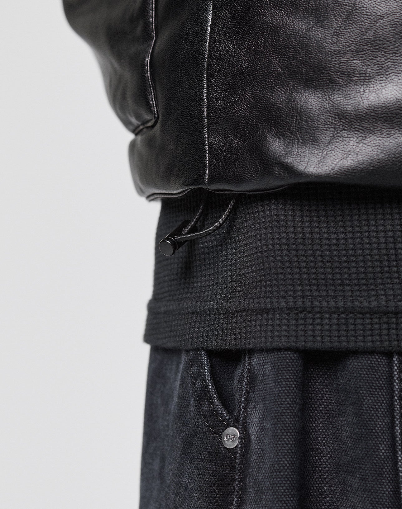 Close-up of the lower section of the LIVE FAST DIE YOUNG Padded Vest featuring a ribbed waistband, visible adjustable drawstring, gepaddeter Stehkragen, and a glimpse of dark textured pants underneath.