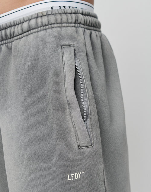 Close-up of a person wearing LIVE FAST DIE YOUNG Basic Loose Jogger in gray, featuring a loose fit, zipper pocket with LFDY logo print, and visible white underwear waistband above the joggers.