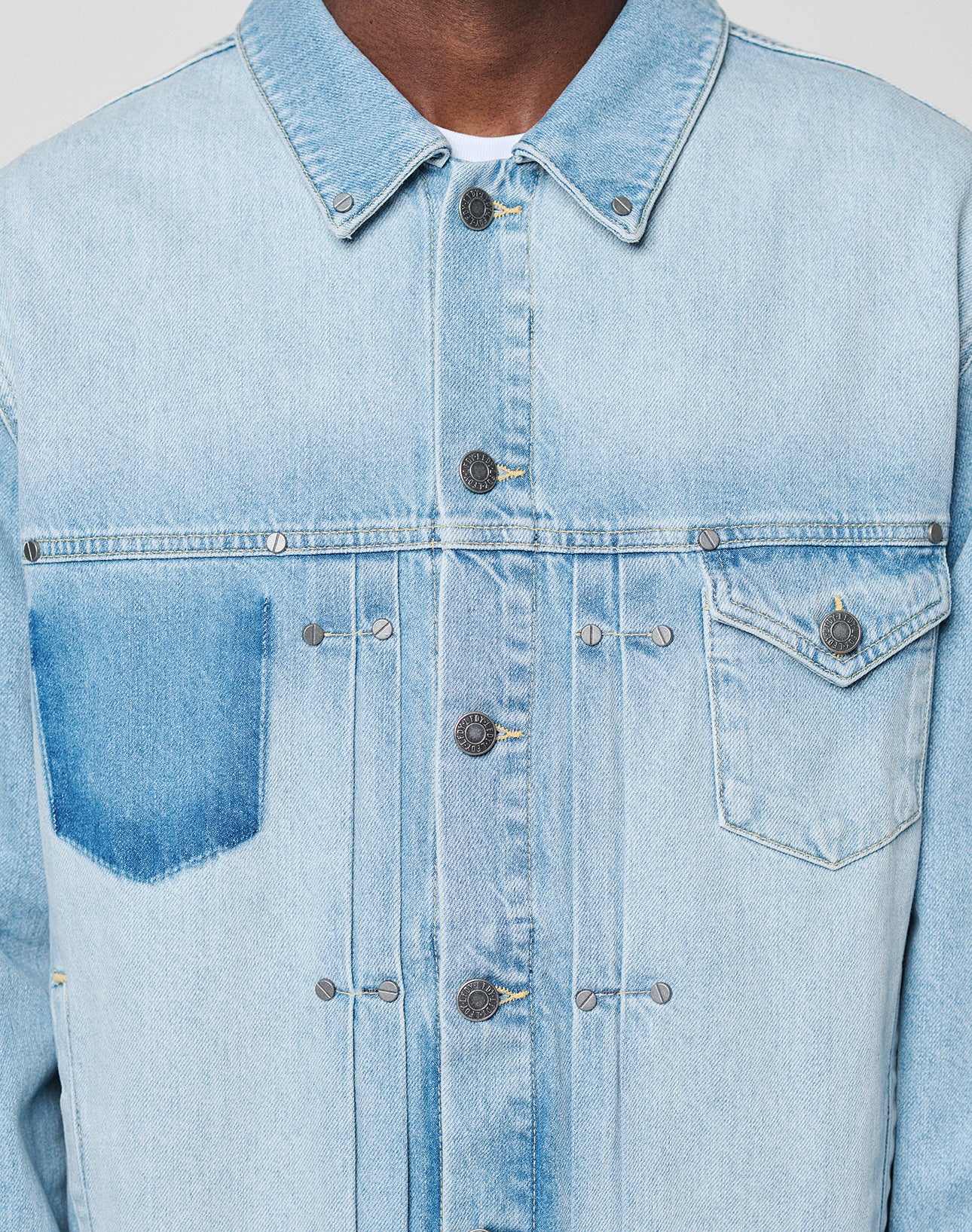 Close-up of the LFDY Trucker Jacket by LIVE FAST DIE YOUNG in light blue denim, Regular Fit, featuring metal buttons and two chest pockets—one with flap, one open. Only the jacket and part of the wearer’s neck are visible.