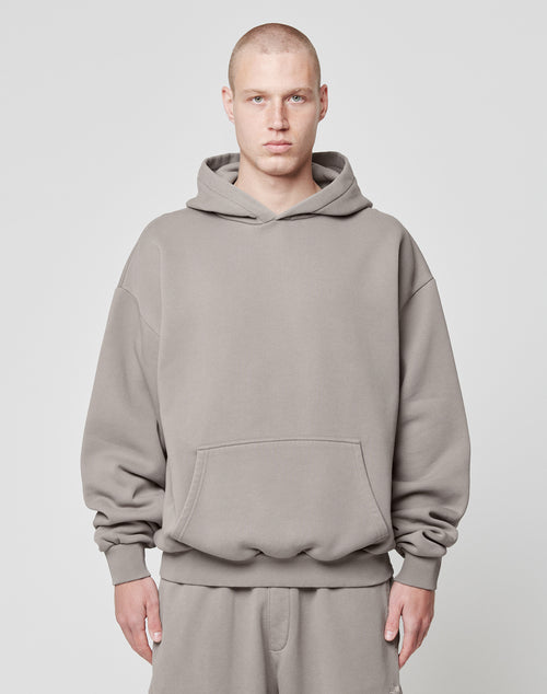 A person with a shaved head wears a taupe LIVE FAST DIE YOUNG Basic Blank Hooded and matching Oversize Fit sweatpants, standing facing forward against a plain light gray background.